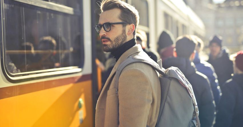 People - Man in Brown Coat and Gray Backpack Posing for a Photo