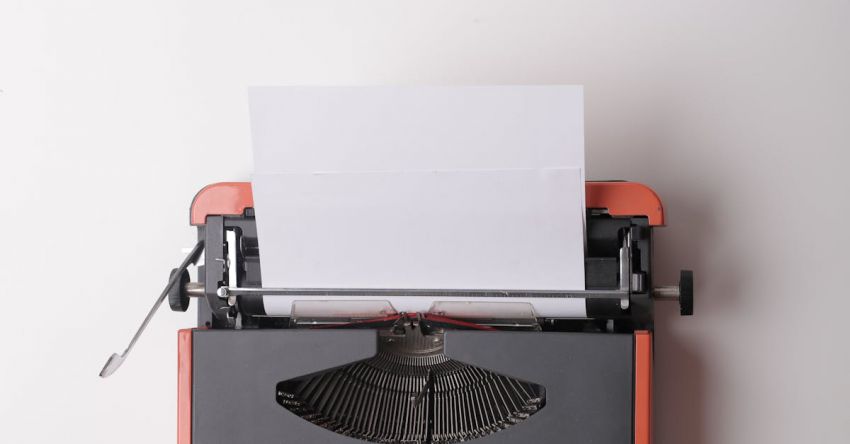 Story - From above crop person using vintage black and red typewriter with white blank sheet of paper against white background